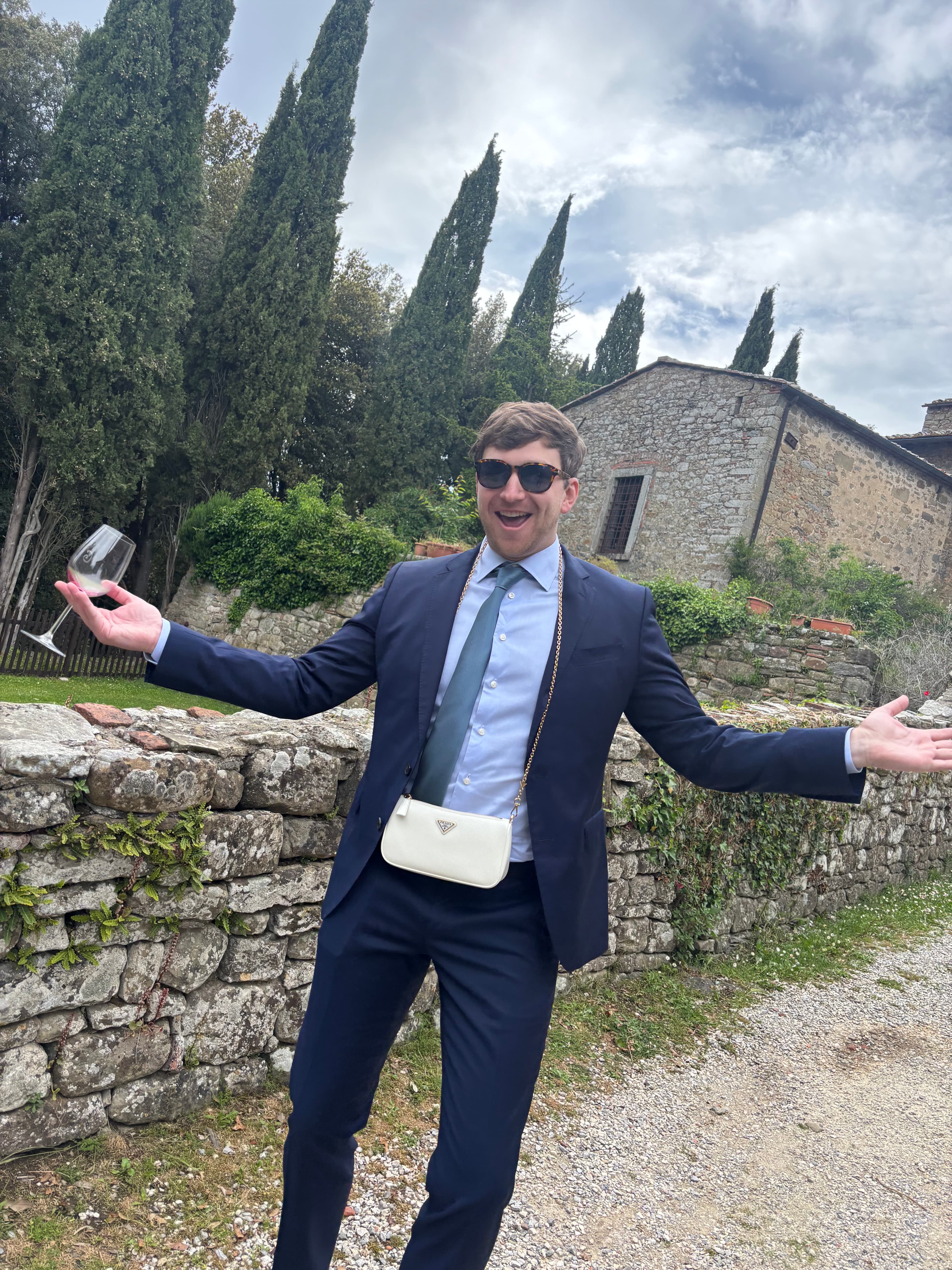 Cole in a suit with wine and a designer bag